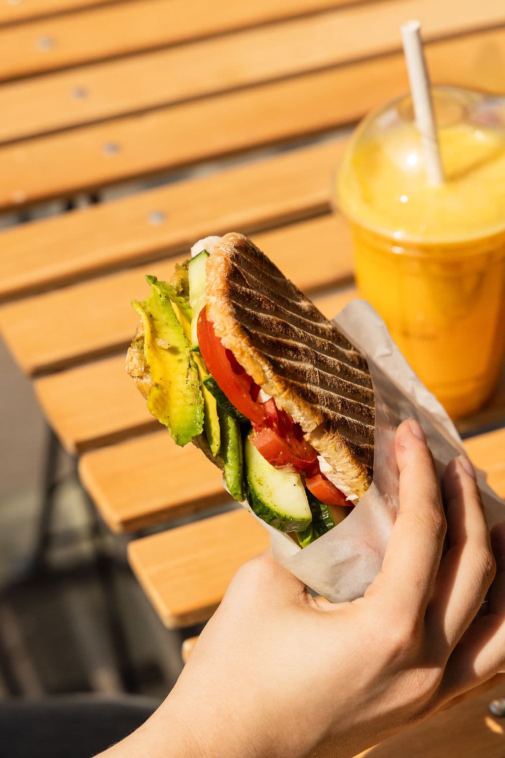 A toasted avocado sandwich held up outside the shop