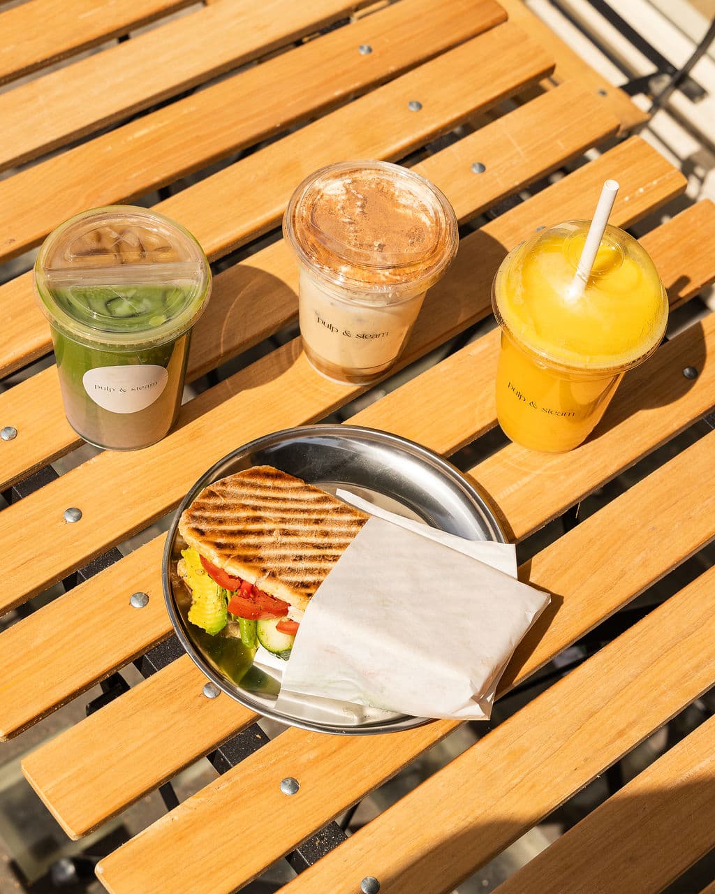 Matcha, coffee, juice and a sandwich spread out on an outside table